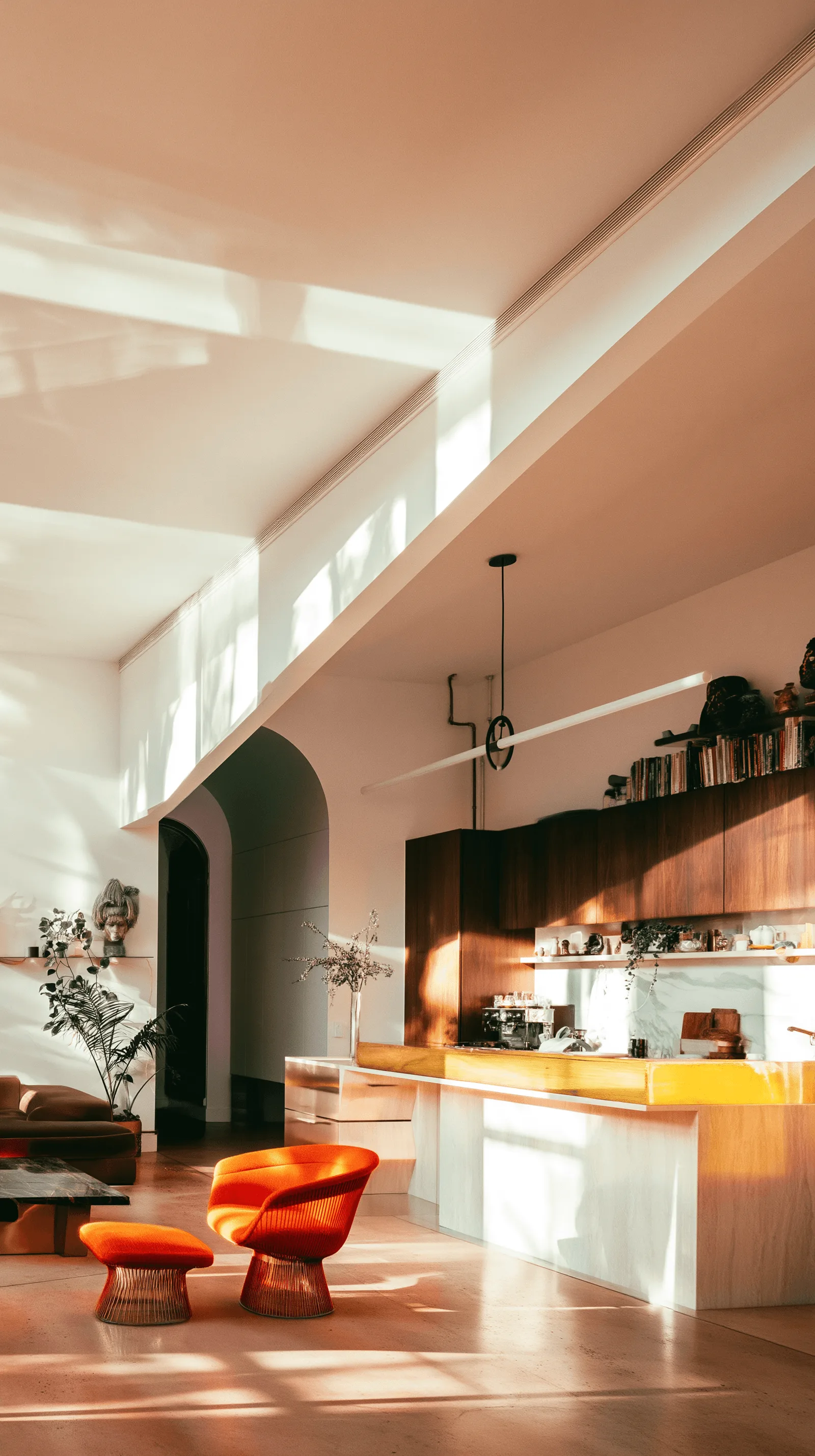A compact kitchen seen through an arched opening, an orange armchair in warm afternoon light